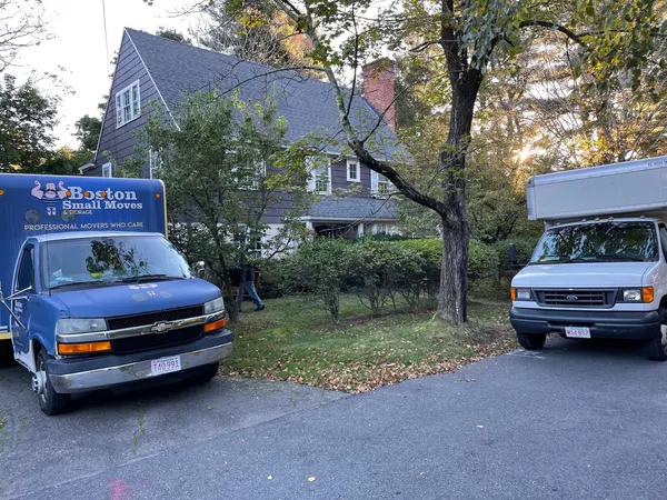 Moving trucks outside a tree-lined New England home