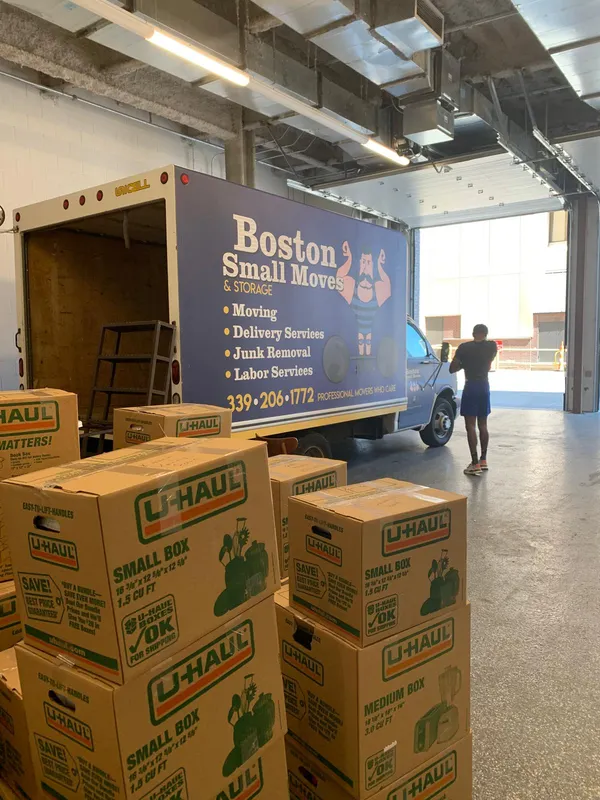Moving boxes stacked beside the Boston Small Moves truck in a loading bay