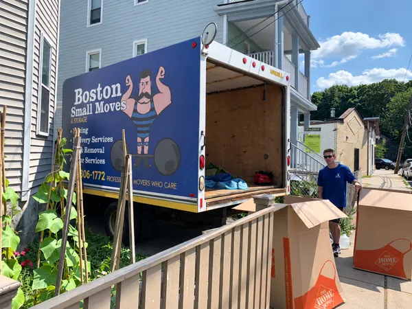 Mover and boxes beside the open moving truck outside a house